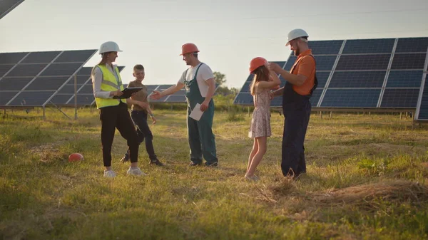 Kaksi pientä lasta juoksee vanhemmilleen, jotka ovat töissä. Aurinkovoimalan työntekijä, jolla on työssä lapsia ja joka hymyilee kameralle. Kolme aurinkoenergian asiantuntijaa aurinkovoimalassa. — kuvapankkivalokuva