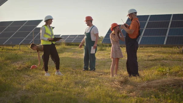 To små barn løper til foreldrene som er på jobb. En ansatt i et solkraftverk med barn på jobb som smiler til kameraet. Tre spesialister på solenergi ved et solkraftanlegg. – stockfoto