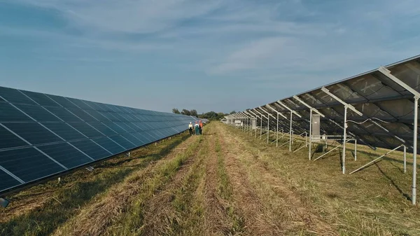 Toppoversikt over spesialister som går over et solkraftverk. Tre ansatte ved alternativt kraftverk som går og snakker om solcelleordning. Samarbeid. Spesialistgruppe. – stockfoto