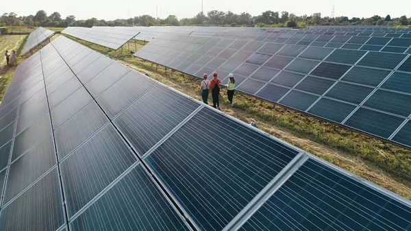 Top näkymä asiantuntijoiden kävely yli aurinkovoimalan. Teollisuusinsinöörien liiketiimi kävelee aurinkotilalla ja keskustelee tehokkaasta rakennussuunnitelmasta. Ekologinen asema. — kuvapankkivalokuva