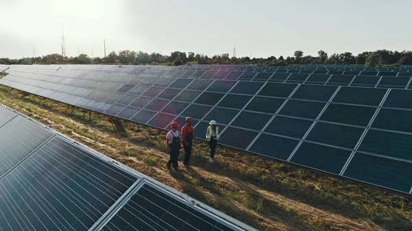 Top view of specialists walking across a solar power plant. Business team of industrial engineers walking on solar farm and discussing efficient plan of construction. Solar energy concept.