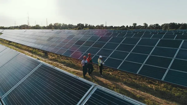 Top view of specialists walking across a solar power plant. Business team of industrial engineers walking on solar farm and discussing efficient plan of construction. Solar energy concept.