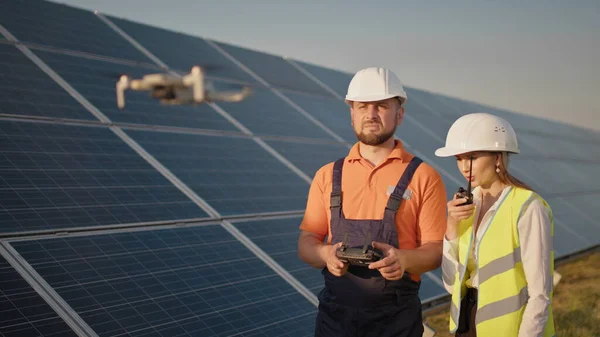 Ipari szakértő visel sisakot és vezérlő drón fotovoltaikus naperőmű. Napelem tömb telepítése. Technológiák és ökológia. A női befektető ellenőrzi a munkát Stock Kép