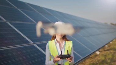 Bir güneş enerjisi santralinin arka planında dron kullanan kadın mühendisin portresi. Güneş paneli kurulumu. Teknoloji ve ekoloji. Gün batımı.