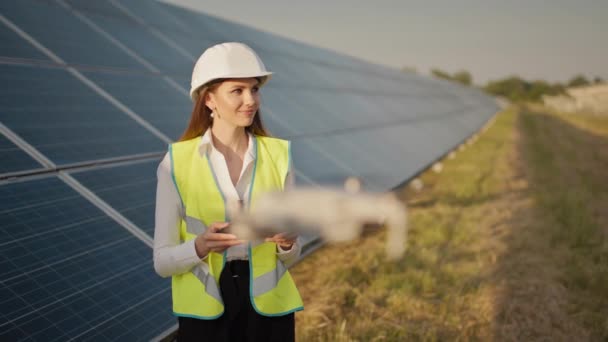 Porträt einer Ingenieurin, die vor dem Hintergrund eines Solarkraftwerks eine Drohne bedient. Photovoltaische Solarpaneelinstallation. Solaranlage. Neue Technologien. Investor und Arbeiter-Ingenieur — Stockvideo