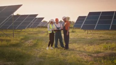 Endüstriyel teknisyenlerden oluşan bir iş ekibi dışarıda güneş parkında yürüyor. Yoğunlaştırılmış güneş enerjisi santralinin yapımı. Yenilenebilir enerji. Ekoloji. Güneş panellerini kontrol eden teknisyen ve yatırımcı