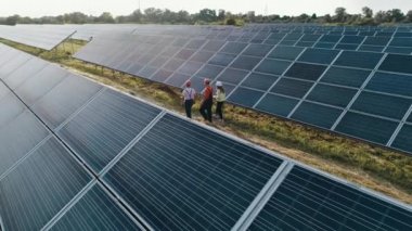Güneş enerjisi santralinde yürüyen uzmanların üst düzey görüntüsü. Endüstriyel mühendislerden oluşan bir iş ekibi güneş çiftliğinde yürüyor ve verimli bir inşaat planı üzerinde tartışıyorlar. Ekolojik istasyon.