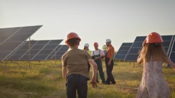 Due bambini piccoli corrono dai loro genitori che sono al lavoro. Un dipendente di una centrale solare con bambini al lavoro che sorridono alla telecamera. Tre specialisti di energia solare in un impianto di energia solare. — Video Stock