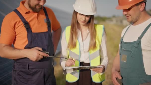 Stazione ecologica. Energia alternativa. Gli ingegneri utilizzano disegni sulla fattoria solare in uniforme speciale sguardo in piedi intorno discutere l'installazione di batterie solari. Settore pannelli solari — Video Stock