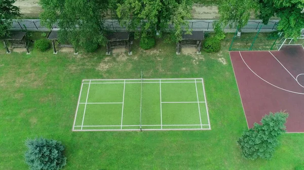 Quadra de grama de tênis vista superior aérea. Tiro aéreo ascendente de quadras de basquete e tênis em um parque urbano americano, à luz da manhã, com longas sombras, capturadas de cima por um drone — Fotografia de Stock