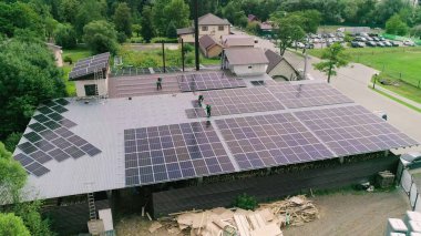 Bir evin çatısına güneş enerjisini elektrik enerjisine çeviren PV güneş panelleri kuran işçiler. İş anlayışı. Özel kıyafetli işçiler yürür ve güneşli hücrelerin kurulumu hakkında konuşurlar