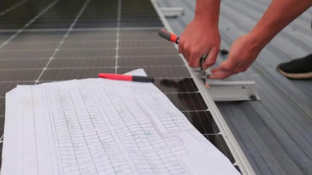 Close-up van de werknemer die het fotovoltaïsche paneelsysteem installeert en onderhoudt. Op de voorgrond ziet men een diagram van de installatie van zonnepanelen. Zonnepanelen op dak. — Stockvideo