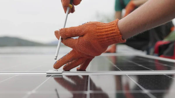 Teknikot asentamassa aurinkopaneeleita metalliseen telineeseen. Työntekijät asentamassa aurinkopaneeleita talon katolle. Lähikuva Aurinkopaneelien asennus, liittäminen ja asennus. Työntekijät kiinnitä aurinkopaneelit — kuvapankkivalokuva