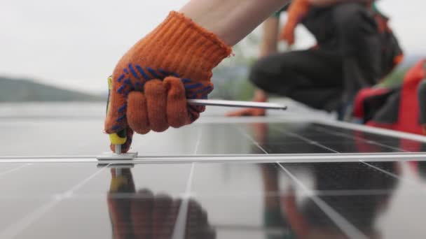 Teknisyenler metal standa güneş panelleri kuruyor. Bir evin çatısına güneş panelleri kuran işçiler. Yakın çekim kurulum, bağlantı ve güneş panellerinin montajı. İşçiler güneş panellerini bağlıyor — Stok video