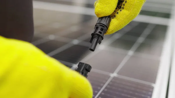 Feche a conexão do cabo elétrico aos painéis solares. Conexão e instalação de painéis solares. Ligação à rede de energia solar. Um eletricista em luvas conecta o cabo — Fotografia de Stock