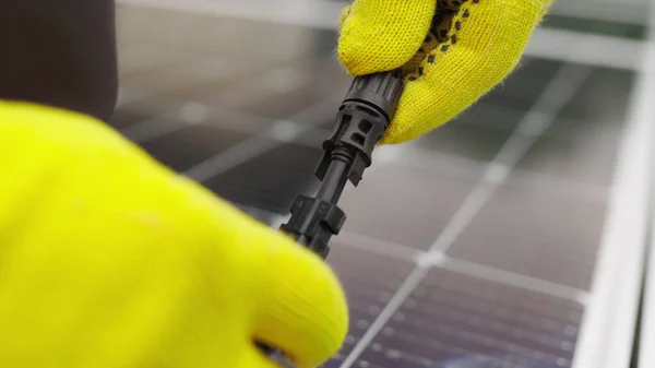 Feche a conexão do cabo elétrico aos painéis solares. Conexão e instalação de painéis solares. Ligação à rede de energia solar. Um eletricista em luvas conecta o cabo — Fotografia de Stock
