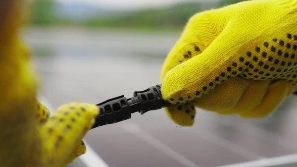 Équipement de la station solaire. Branchement de fils de panneaux solaires à une ferme solaire. Les ingénieurs connectent le système électrique à l'extérieur sur un fond de panneaux solaires. Travailleur dans des gants de protection connecte le fil — Photo