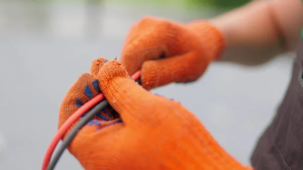An electrician worker holds a red and black high-voltage electric cable, checks the quality of the cables. Connecting electrical cables. Close up of male hands in protective gloves holding cable
