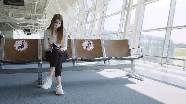 Femme d'affaires confiante dans un masque assis à l'aéroport, tenant un passeport et des billets d'avion, garde une distance en cas de pandémie. J'attends à l'aéroport. Concept de voyage pandémique. Distance sociale — Photo
