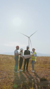 Mühendis ve mimarlardan oluşan bir ekip, güneşli bir günde sürdürülebilir enerjiyi tartışan bir rüzgar türbininin planlarını gözden geçiriyorlar..