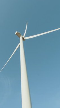 Rüzgâr türbininin düşük açılı görüntüsü açık mavi gökyüzüne karşı keskin bıçaklarla yenilenebilir enerji sergiliyor..