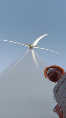 İki mühendis rüzgar türbini önünde el sıkışıyor, işbirliğini ve yenilenebilir enerjiyi sembolize ediyorlar..