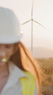 Sert şapka ve güvenlik gözlüğü takan kadın bir mühendis açık havada, muhtemelen inşaat alanında veya endüstriyel bir ortamda bir tablet kullanıyor. Dikey video.