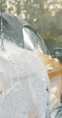 Köpüklü sabunla yıkanan bir arabanın dikey çekimi. Kabarcıklar aracın kenarından taşar. Araba temizleniyor..