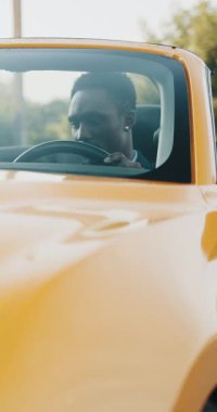 Şık bir siyah adam üstü açık bir araba kullanıyor, açık yolların tadını çıkarıyor. Dikey video.