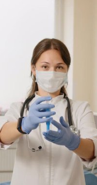 Maske ve eldiven takan bir tıp uzmanı enjeksiyon için şırınga hazırlıyor. Bu dikey görüntü, sağlık hizmetleri ve aşılara odaklanmayı yakalar.