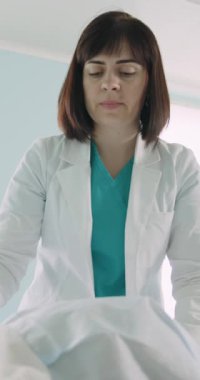 Beyaz önlüklü bir kadın doktor bir hastayı muayene ediyor, klinik bir ortamda tıbbi bakıma odaklanıyor. Dikey video.