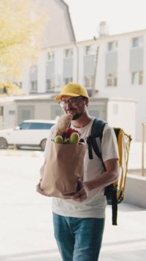 Sarı şapkalı ve gözlüklü bir teslimatçı kameraya el sallıyor..