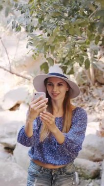 Şapka takan bir kadın dışarıda eğlenirken telefonuyla fotoğraf çekiyor. Dikey video.