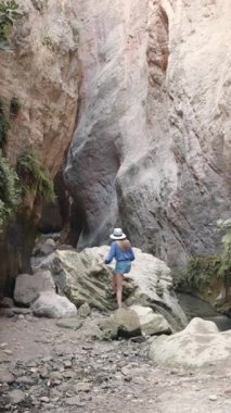 Bir kadın dar bir kanyonda büyük bir kayaya tırmanıyor, dikey video formatında macera ve keşif sergiliyor..
