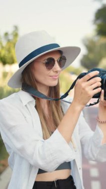 Şapka takan ve güneş gözlüğü takan bir kadın park ortamında fotoğraf çekiyor..