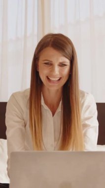 Bir kadın dizüstü bilgisayarına bakarken şaşkınlıkla yüzünü kapatıyor. Parlak bir odada, bir yatakta oturuyor..