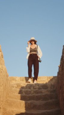 Şapkalı ve günlük kıyafetli bir kadın güneşli bir günde antik taş basamaklardan iniyor..