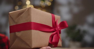 Güzel paketlenmiş kırmızı kurdeleli bir hediye özel birine verilmeye hazır. Bir insan, Noel ağacının önünde kırmızı kurdeleyle paketlenmiş bir hediye sunar.