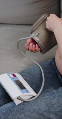 Kişi koltukta otururken kolundaki dijital monitörle evdeki kan basıncını ölçer.