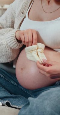 Kanepede kot pantolon ve süveter giyerek otururken beyaz kumaşı iğne ve iplikle diken kadınların yakın çekimi.