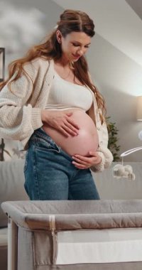 Hamile kadın yeni bir hayat ve annelik beklentisiyle bir beşiğe bakarken karnını nazikçe eğiyor.