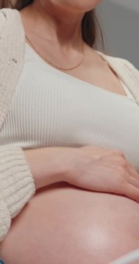 Hamile kadınların göbeğini ve ellerini üzerine koyup, kot pantolon giyip, ön planda yumuşak odaklı oyuncaklar giyiyorlar.