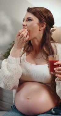 Koca göbekli hamile kadın elinde bir bardak kırmızı meyve suyu, yakınlarda bir tabak elma, rahat kıyafetler, gevşemiş ruh hali.