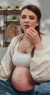 Hamile kadın kanepede oturup kaseden patlamış mısır yiyor, evde dinleniyor.