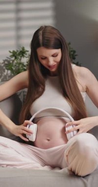 Gülümseyen hamile kadın, doğmamış bebeğine müzik dinlemek için karnına kulaklık takıyor.