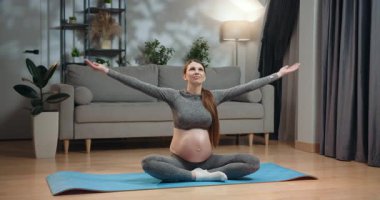 Rahat giyimli hamile bir kadın yoga minderinde bacak bacak üstüne atarak oturur, dua pozisyonunda ellerini birbirine bastırarak meditasyon yapar, gözleri kapalı, evde iç huzuru bulur. Hamile Kadın Meditasyon