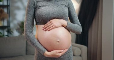 Hamile bir kadın kulaklık takıyor ve oturma odasında durup müzik dinlerken karnına dokunuyor ve anneliği bekliyor. Hamile Kadın Müzik Dinliyor