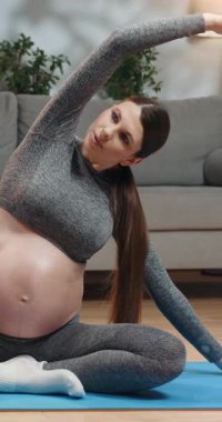 Spor giyim sektöründe hamile bir kadın oturma odasında vücudunu yoga minderine dayayıp hamilelik süresince sağlığına odaklanıyor.