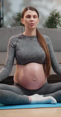 Spor kıyafetleriyle meditasyon yapan hamile bir kadın. Gözleri nilüferde kapalı. Mavi yoga minderinde poz veriyor.