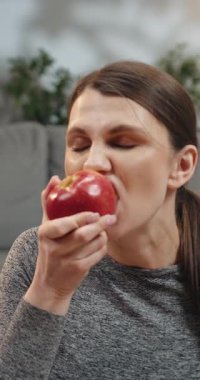 Gri bluzlu hamile kadın kırmızı elma yiyor, karnını ve yüzünü kapatıyor, hamilelik sırasında sağlıklı atıştırıyor.